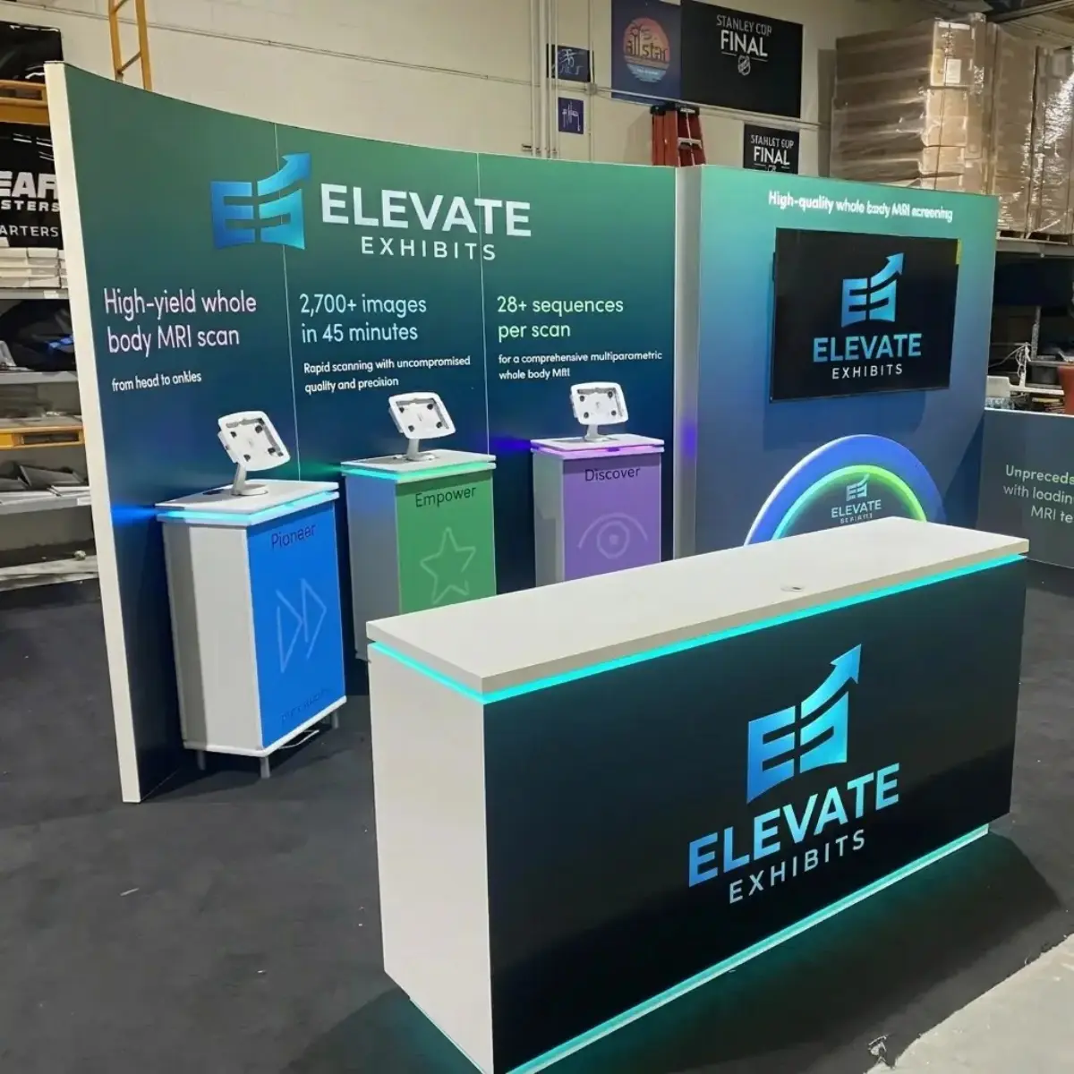 Trade show booth design by Elevate Exhibits featuring interactive displays for MRI scanning technology, showcasing Pioneer, Empower, and Discover with branding elements and modern aesthetics.