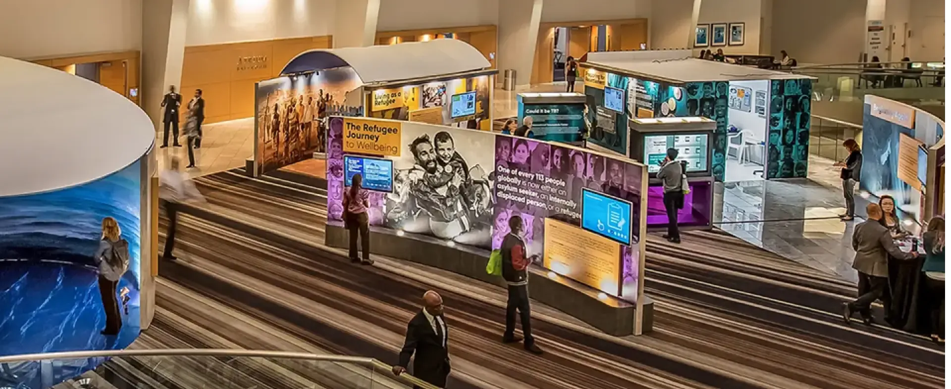 Trade show booth setup featuring interactive exhibits on refugee experiences, with attendees engaging and multimedia displays, showcasing Elevate Exhibits design and logistics capabilities.