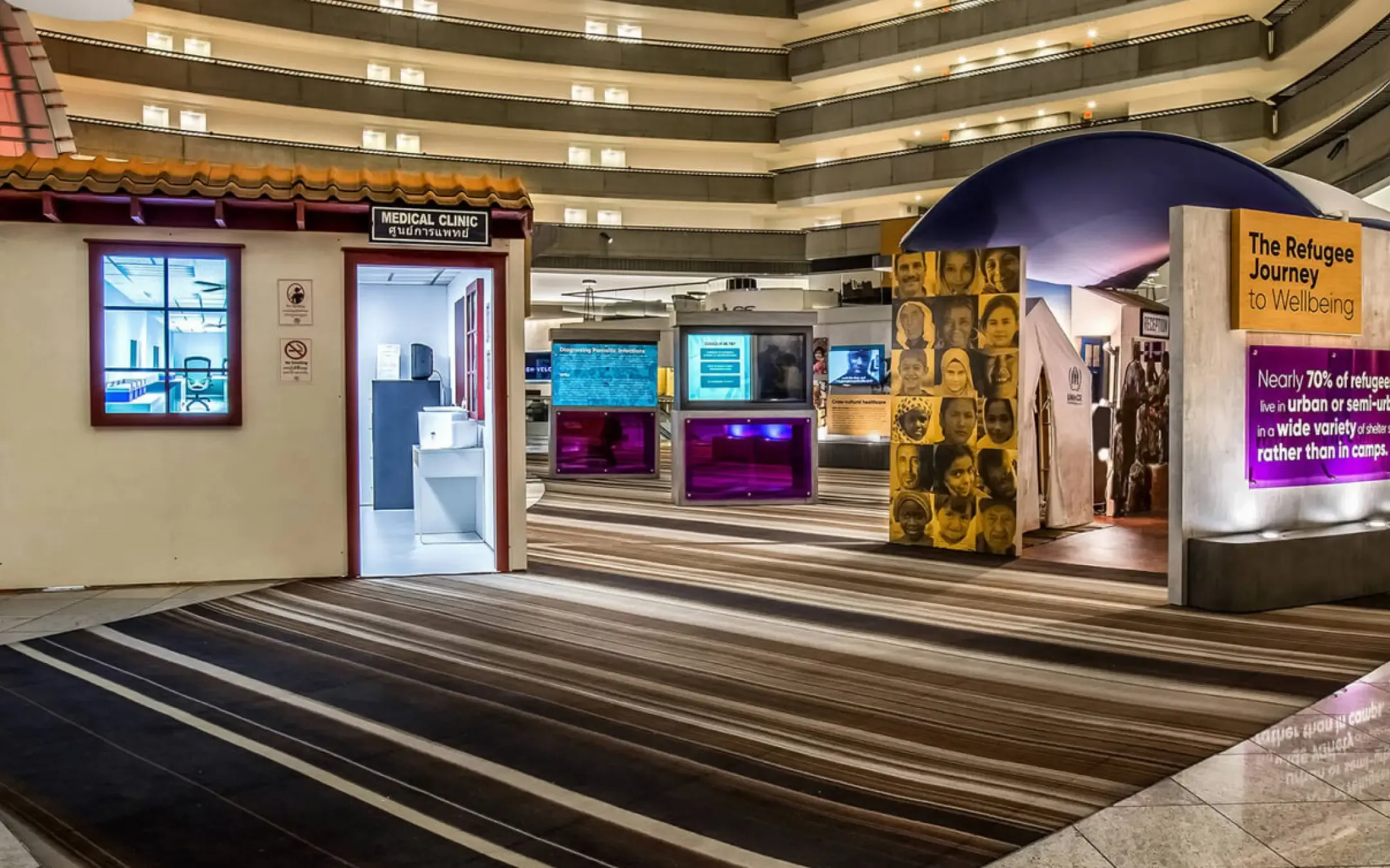Trade show exhibit featuring a medical clinic display and a The Refugee Journey to Wellbeing installation, showcasing informational panels and visuals on refugee health and urban living.